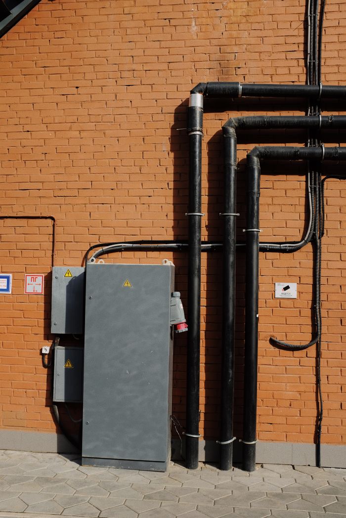 Outdoor scene showing electrical pipes and power box mounted on a brick wall.